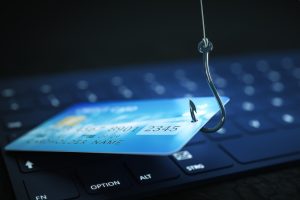 An image of a credit card with a small hole on one end and a fishing hook and line lifting it off a keyboard.