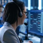 A person with a headset looks at a computer while helping a client on the phone.