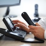 A person is dialing a number on a VoIP phone at their desk.