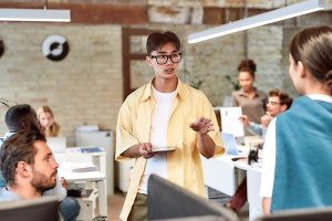 A team leader in a yellow shirt talking to fellow employees in an office.