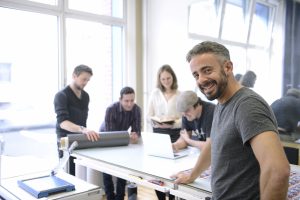 A man is looking at the camera with employees in the background smiling and doing work.