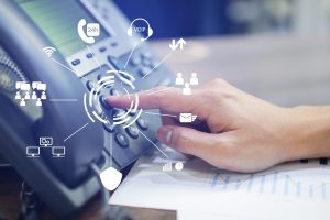 A finger touching a button on a desktop phone with VoIP icons over the top.