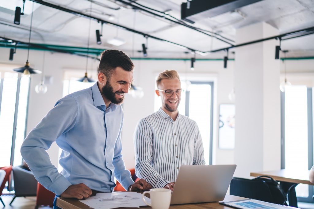 Two people using a laptop at work and smiling.