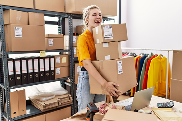 A woman carrying stacks of boxes for shipping at her small business.