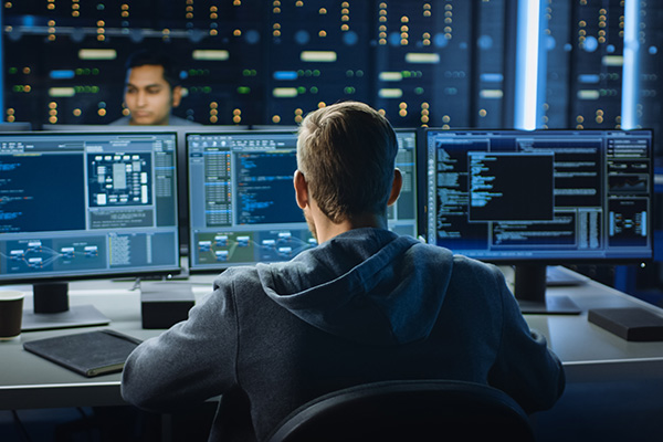 An IT professional sitting in front of three computer screens to monitor networks.