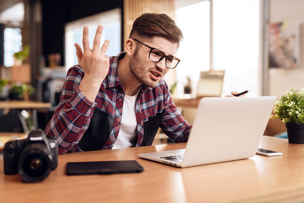 A man in a flannel shirt expresses frustration at his laptop.